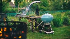 A blue Weber kettle grill next to a Weber travel grill in a garden
